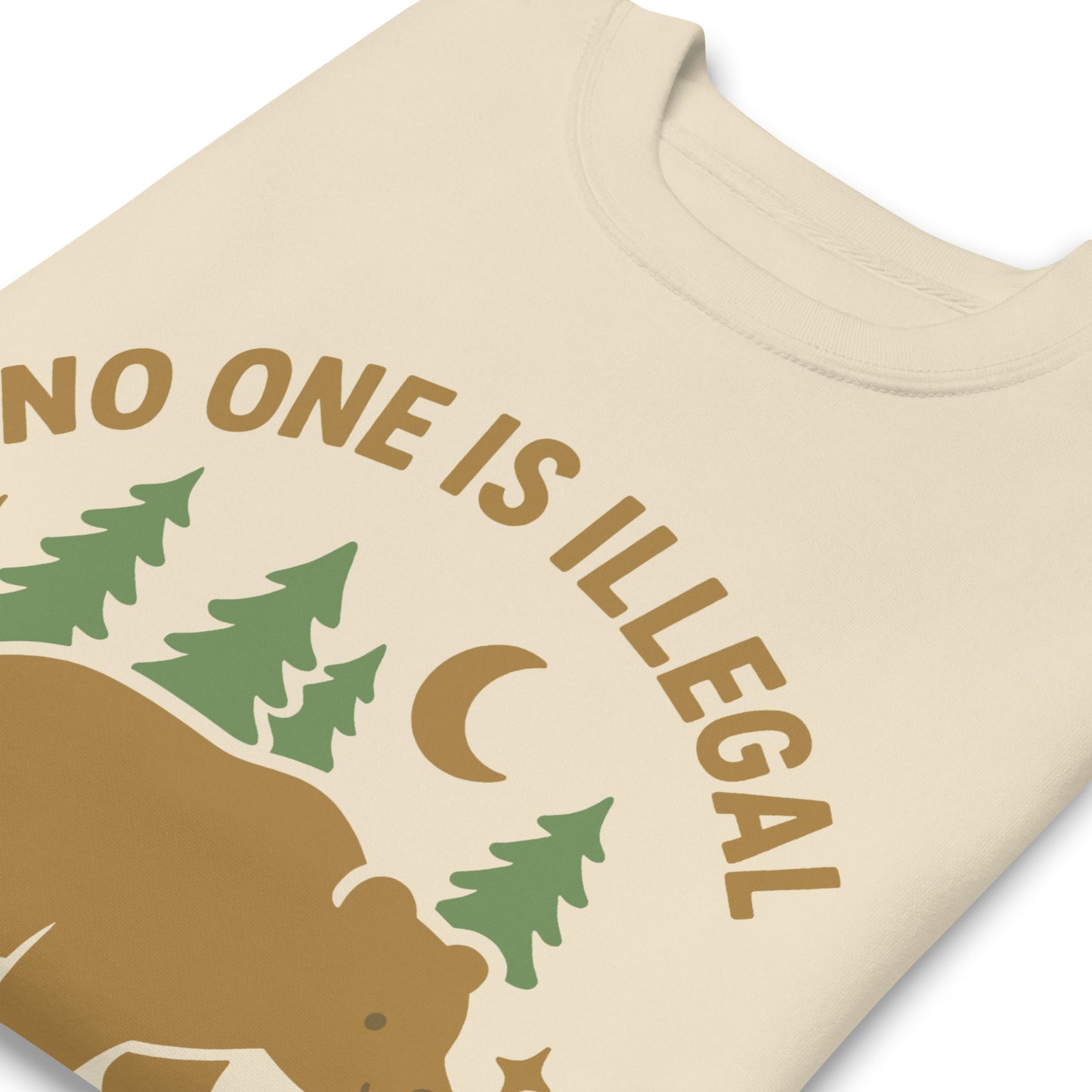 Close-up of a cream unisex premium sweatshirt highlighting the bear, trees, and moon graphic and the message “NO ONE IS ILLEGAL ON STOLEN LAND,” shown in warm earthy print tones.