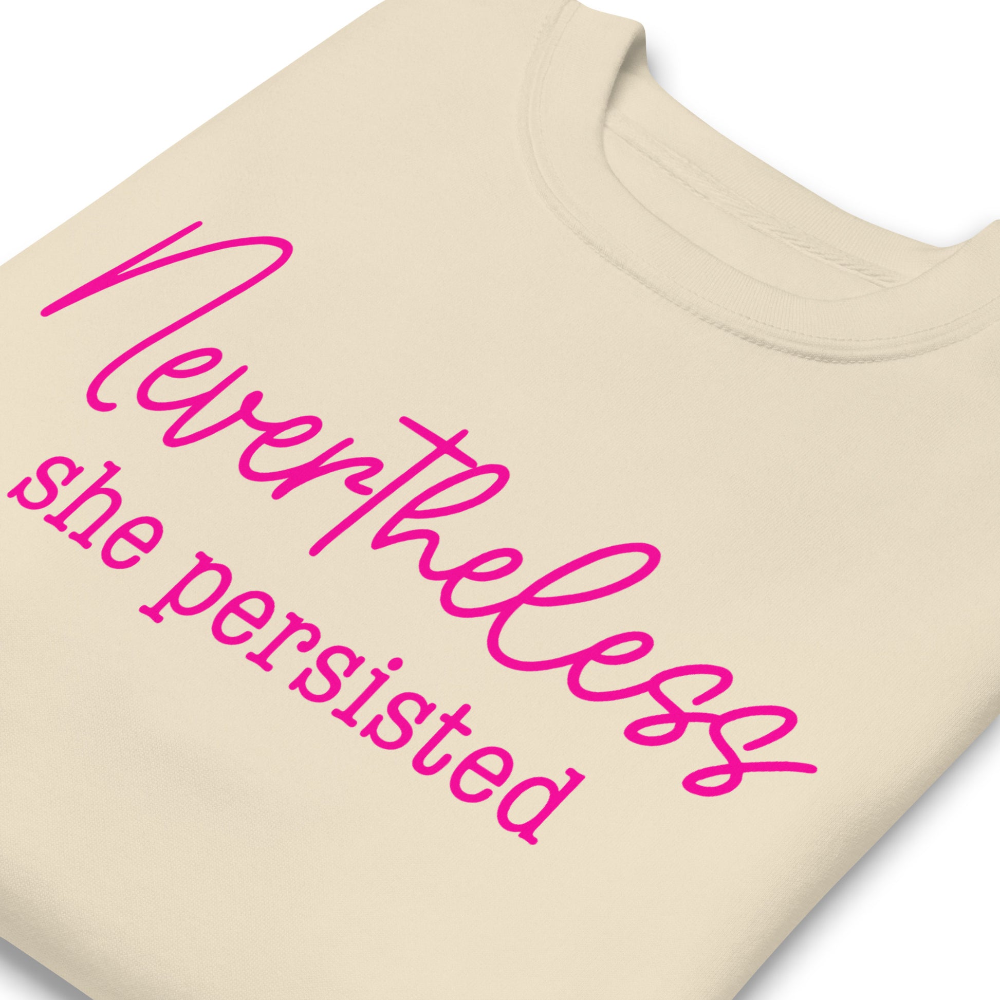 Sand unisex premium sweatshirt close-up featuring pink script text “Nevertheless she persisted,” women’s empowerment statement apparel.