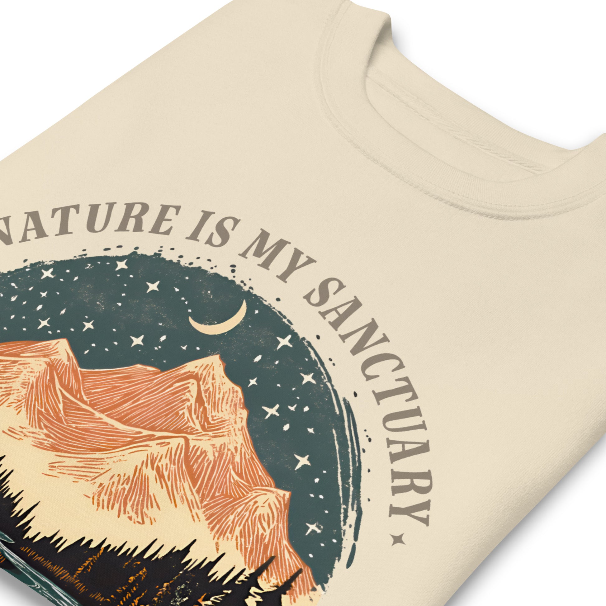 Close-up cream sweatshirt print showing scenic mountain artwork with pine trees, river, and “The Earth Is My Temple” phrase in outdoor design.