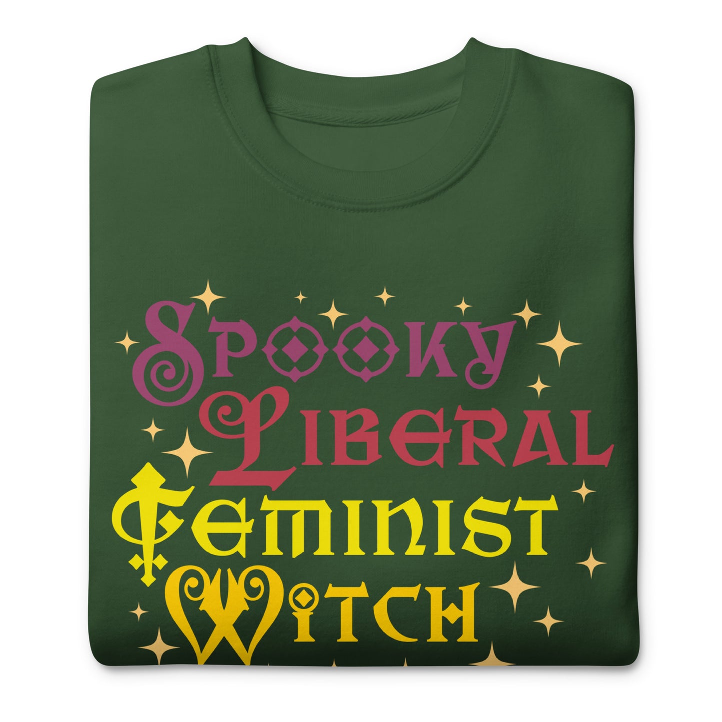 Folded forest green unisex premium sweatshirt featuring whimsical stacked lettering with star accents, bright contrasting colors, centered design, printed message “SPOOKY LIBERAL FEMINIST WITCH.”