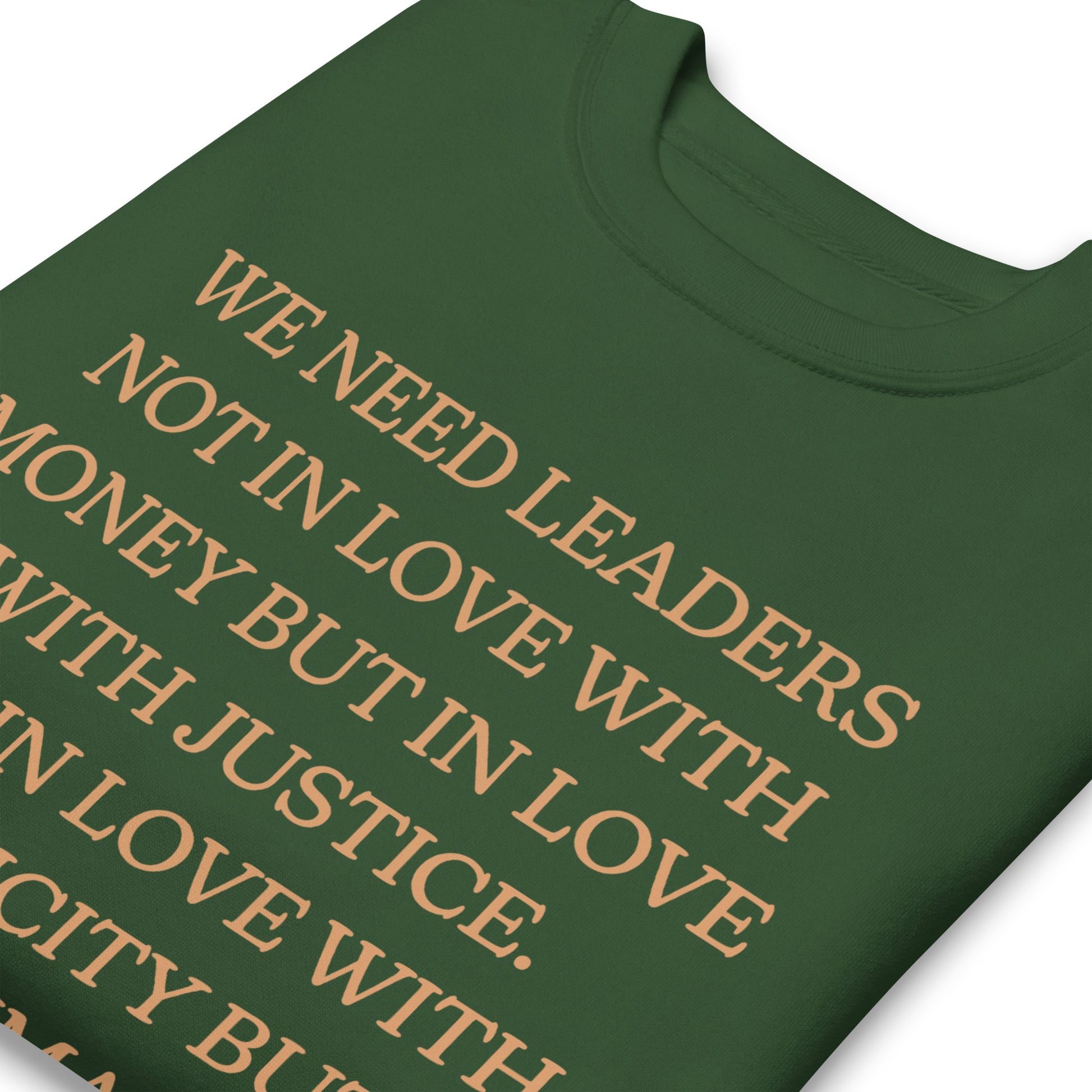Close-up of a forest green unisex premium sweatshirt showing the MLK quote arranged in centered gold text, highlighting justice-focused leadership and humanity.