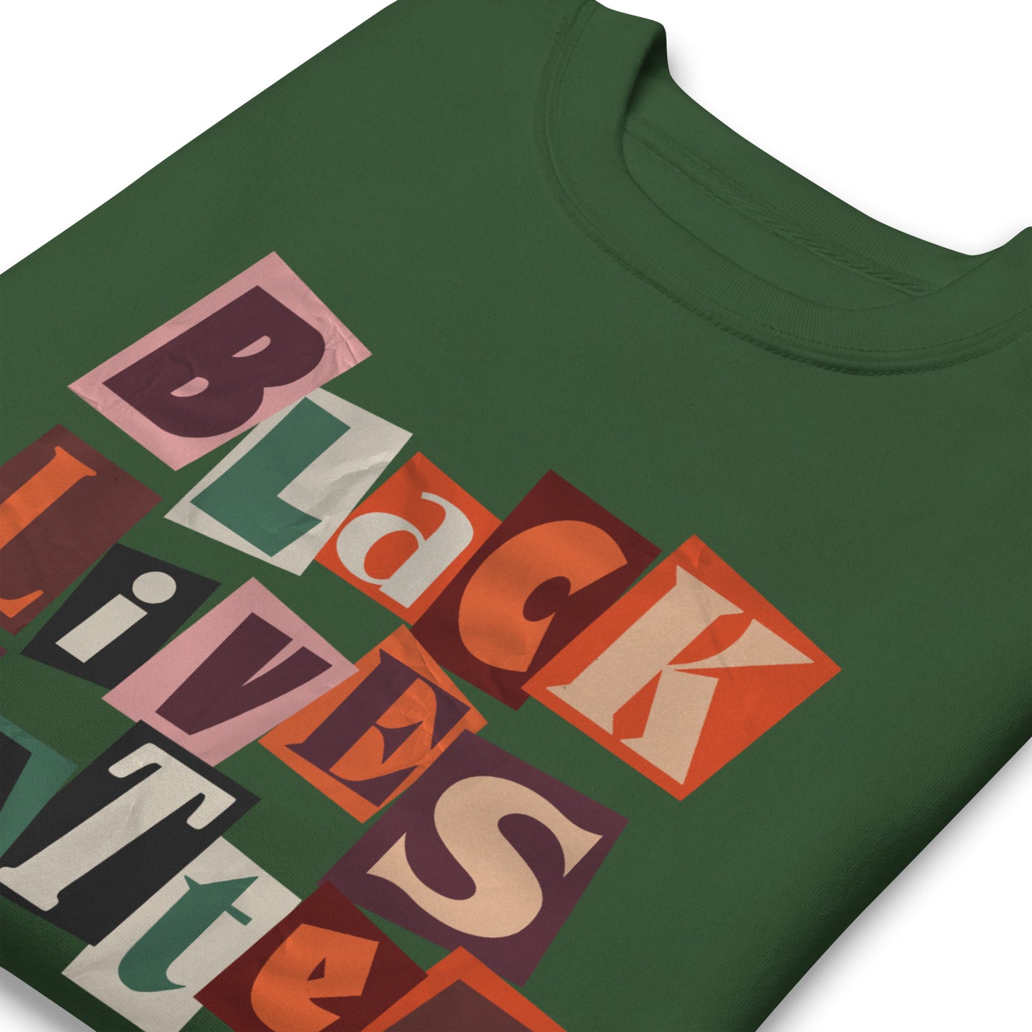 Close-up of a forest green premium sweatshirt showing the colorful cut-paper “BLACK LIVES MATTER” collage text and the smaller “JUSTICE. EQUALITY. NOW.” statement beneath.