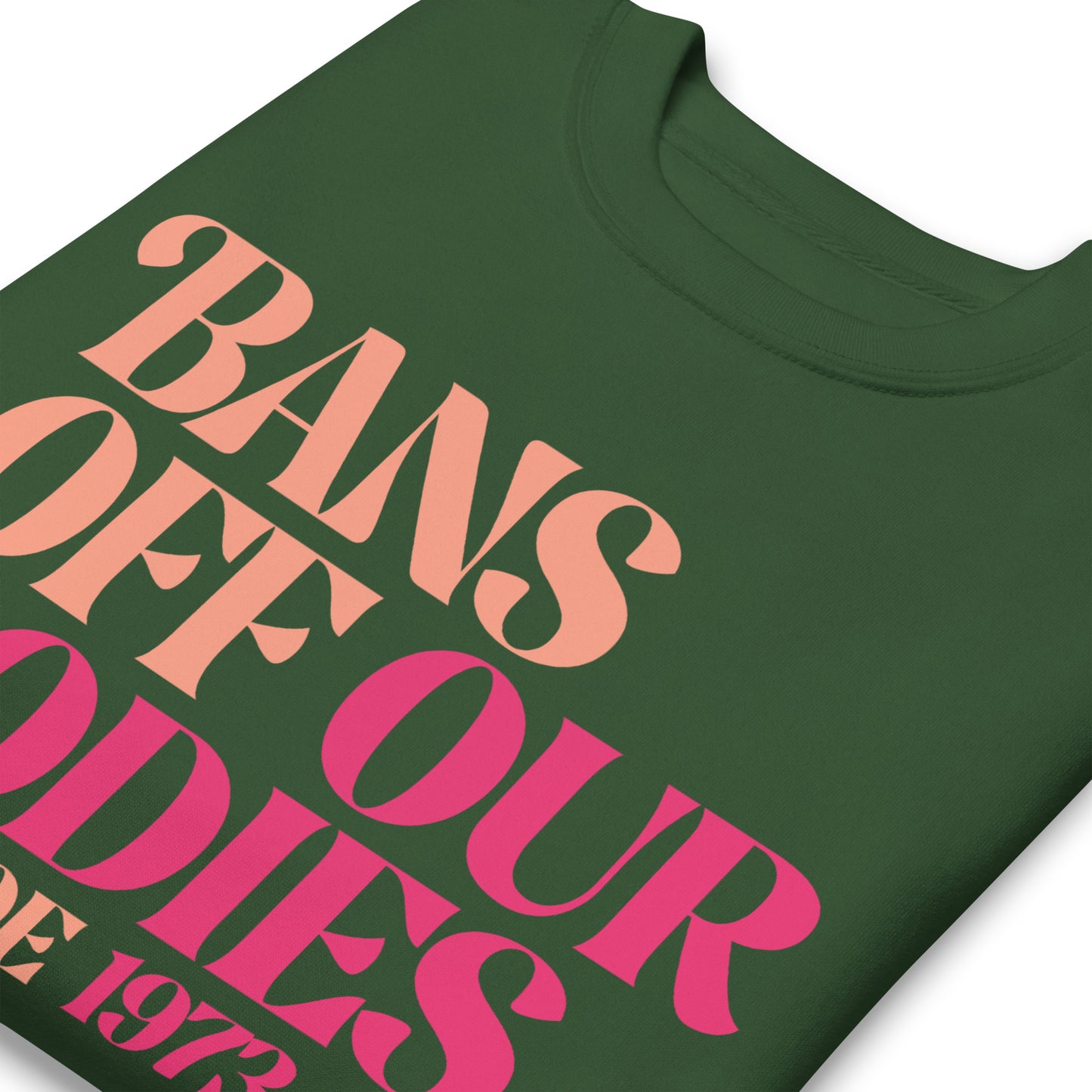 Close-up of forest green unisex premium sweatshirt showing retro serif lettering in pink gradient, stacked typographic layout, printed message “BANS OFF OUR BODIES PRO ROE 1973.”