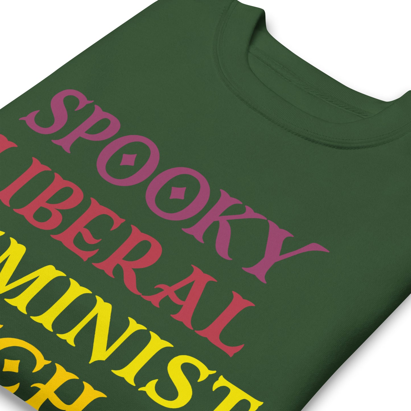 Close-up of forest green unisex premium sweatshirt showing stacked retro typography in contrasting colors, bold letterforms and smooth print texture, printed message “SPOOKY LIBERAL FEMINIST WITCH.”