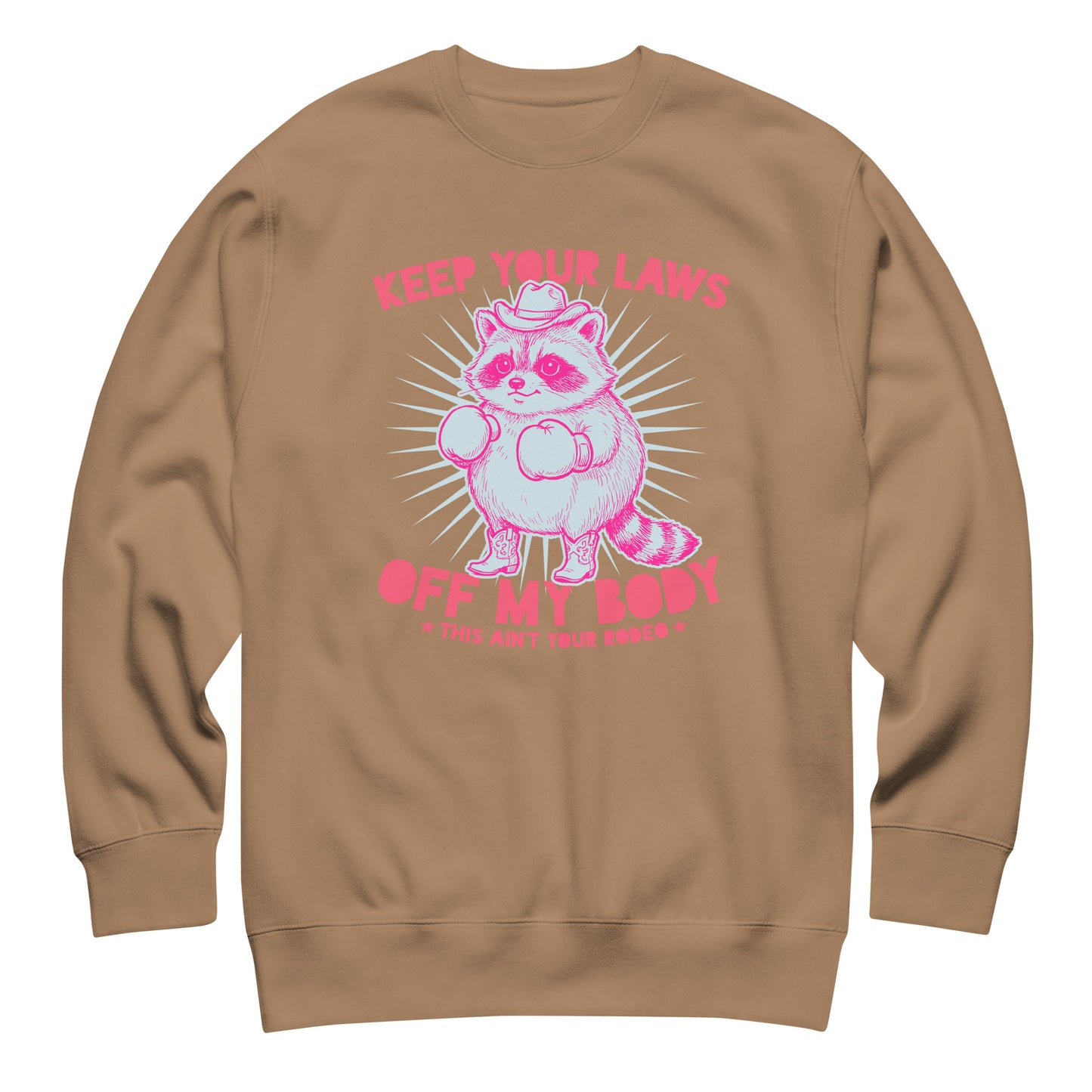 Latte brown unisex premium sweatshirt displaying pink raccoon cowboy graphic with “Keep Your Laws Off My Body” phrase in western activist style.