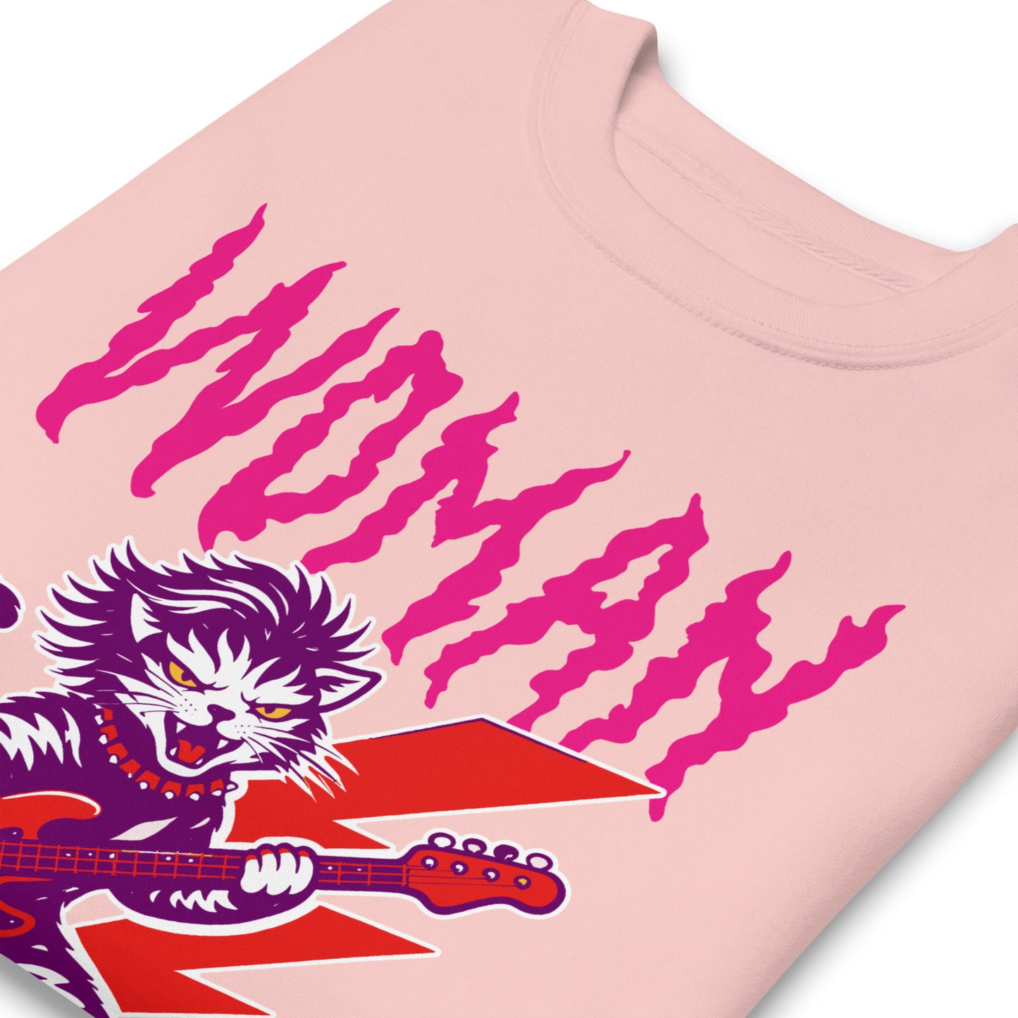 Close-up of a light pink unisex premium sweatshirt highlighting distressed pink typography reading “WOMAN OF A CERTAIN RAGE,” with partial view of the punk rock cat illustration.