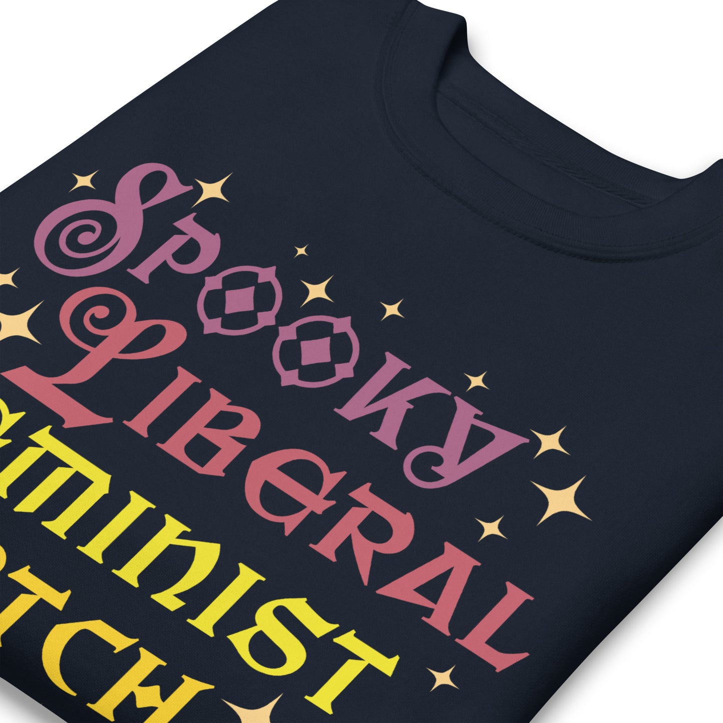 Close-up of navy unisex premium sweatshirt showing sparkly star details around stacked typography, smooth print texture, playful Halloween aesthetic, printed message “SPOOKY LIBERAL FEMINIST WITCH.”