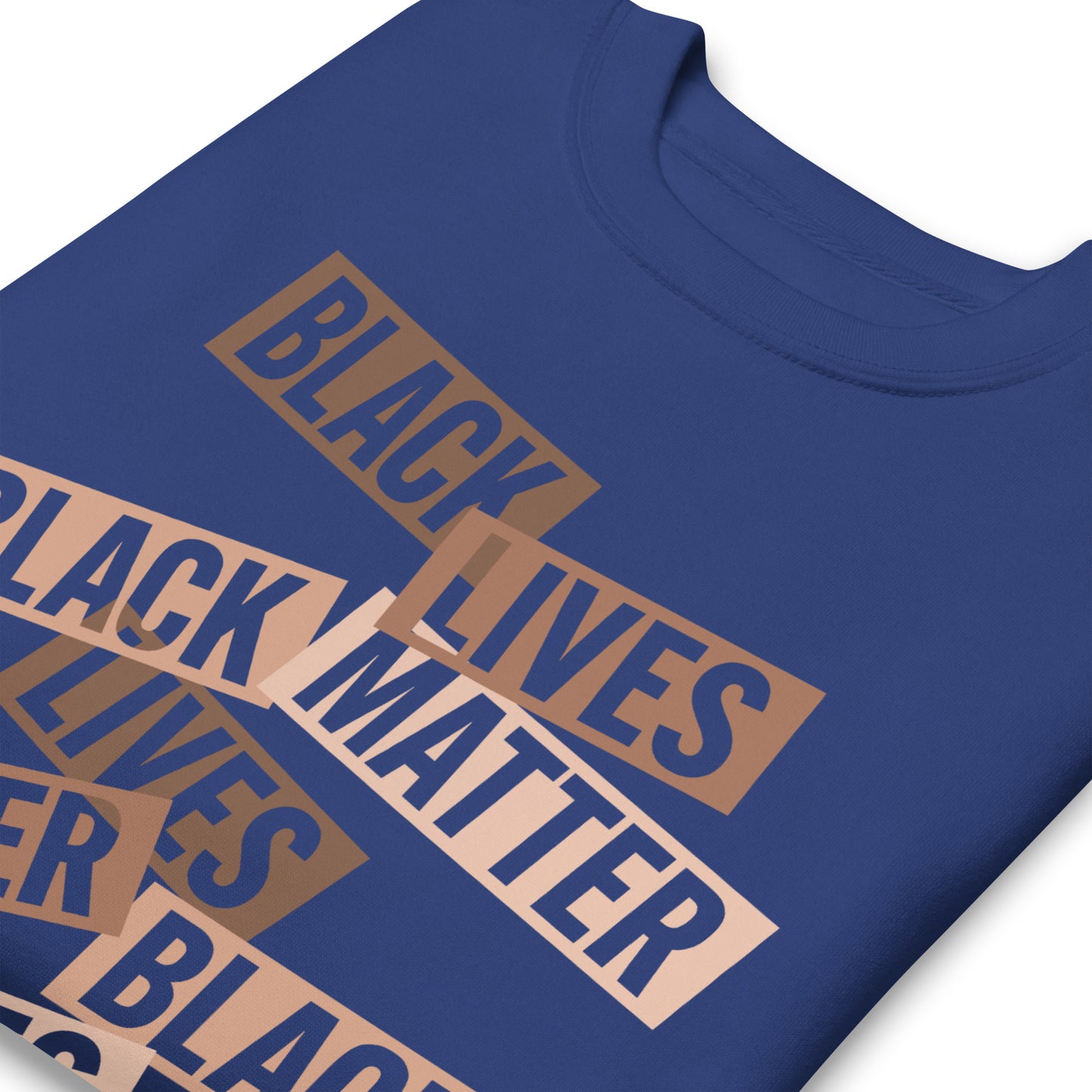 Close-up of a blue sweatshirt displaying angled brown cut-paper word strips that read “BLACK LIVES MATTER.” Textured layout emphasizes a strong racial-justice message.