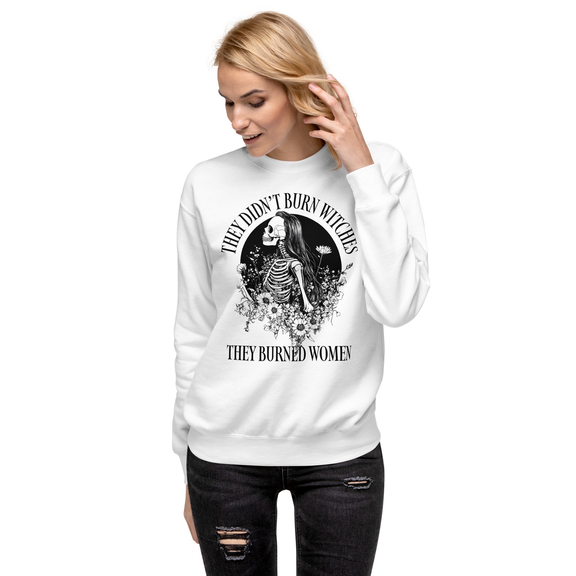 Model wearing white unisex premium sweatshirt with ornate skeleton illustration and arched typography, centered gothic design, printed message “THEY DIDN’T BURN WITCHES THEY BURNED WOMEN,” feminist apparel from Blue Wave USA.