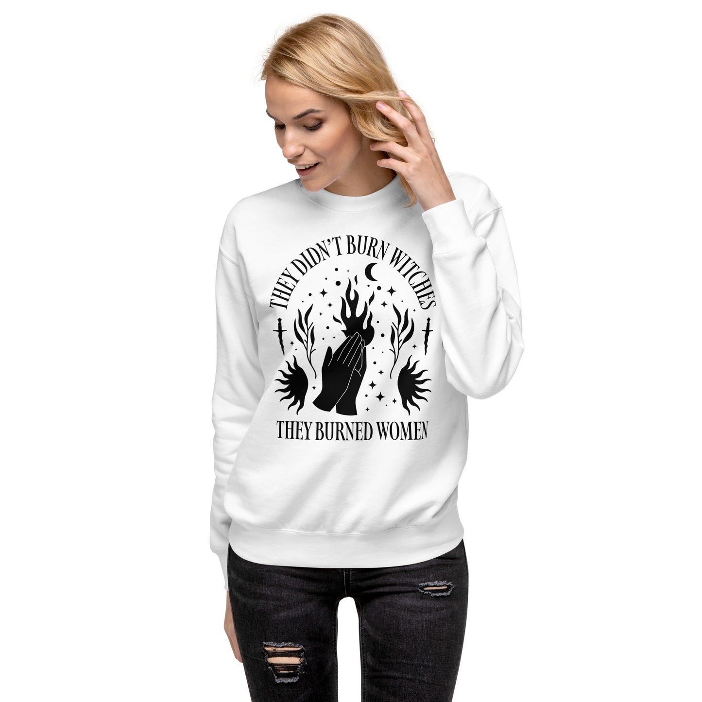 Model wearing white unisex premium sweatshirt with high-contrast occult illustration of raised hands and flames, centered gothic design, printed message “THEY DIDN’T BURN WITCHES THEY BURNED WOMEN.”