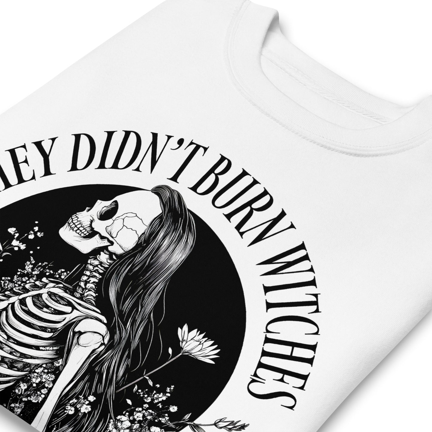 Close-up of white unisex premium sweatshirt showing detailed witch and skeleton illustration, fine linework and textured print, printed message “THEY DIDN’T BURN WITCHES THEY BURNED WOMEN.”