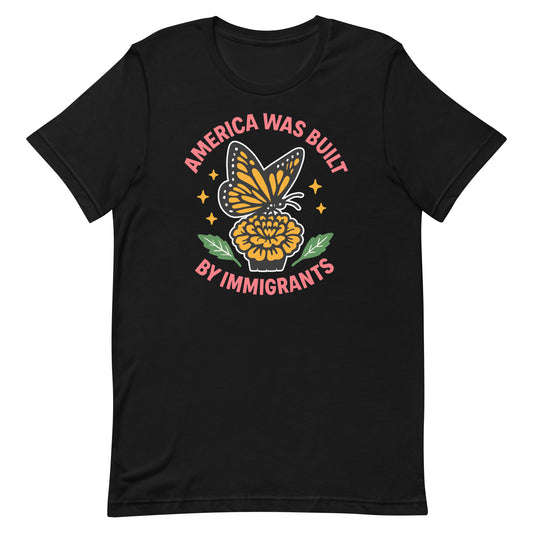 Black “America Was Built by Immigrants” shirt with monarch butterfly and yellow flower graphic, progressive activist tee celebrating diversity.