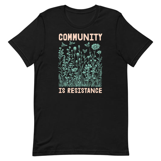 Black unisex t-shirt with a detailed mint-green wildflower illustration beneath bold text reading “COMMUNITY IS RESISTANCE.” A nature-inspired design symbolizing unity, growth, and collective action.