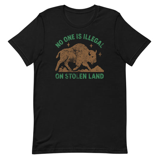 Black unisex t-shirt featuring an earthy buffalo silhouette with stars and the message “NO ONE IS ILLEGAL ON STOLEN LAND,” a bold Indigenous rights design in muted brown and green tones.