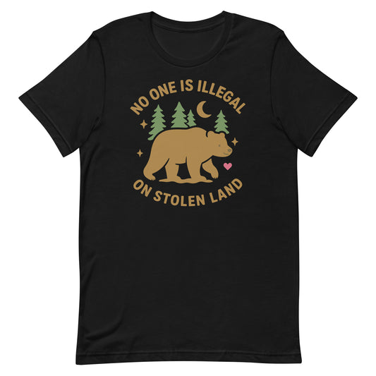 Black unisex t-shirt featuring a tan bear with trees, stars, and moon, along with the message “NO ONE IS ILLEGAL ON STOLEN LAND,” printed in earthy tones.