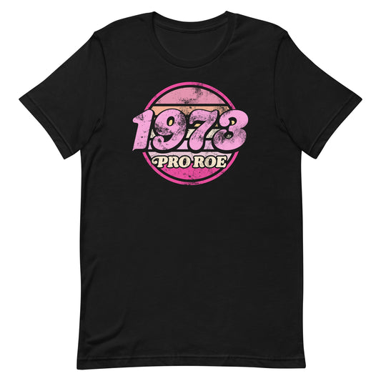 Black unisex t-shirt featuring a distressed retro circular badge design in pink and cream reading “1973 PRO ROE,” vintage protest graphic centered on a solid black garment.