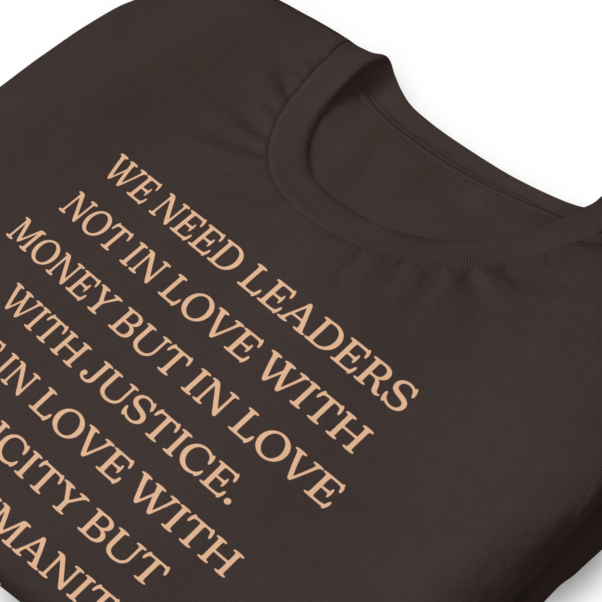 Close-up of a brown shirt showing the MLK quote: “WE NEED LEADERS NOT IN LOVE WITH MONEY… JUSTICE… NOT IN LOVE WITH PUBLICITY BUT WITH HUMANITY.” Soft serif typography highlighting civil-rights messaging.