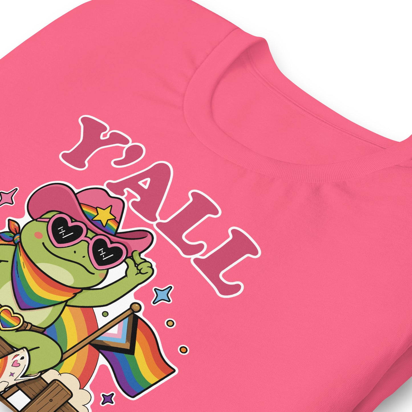 Close-up of pink pride t-shirt featuring rainbow cowboy frog artwork, pride flag details, western-inspired styling, and inclusive “Y’All Means All” typography.