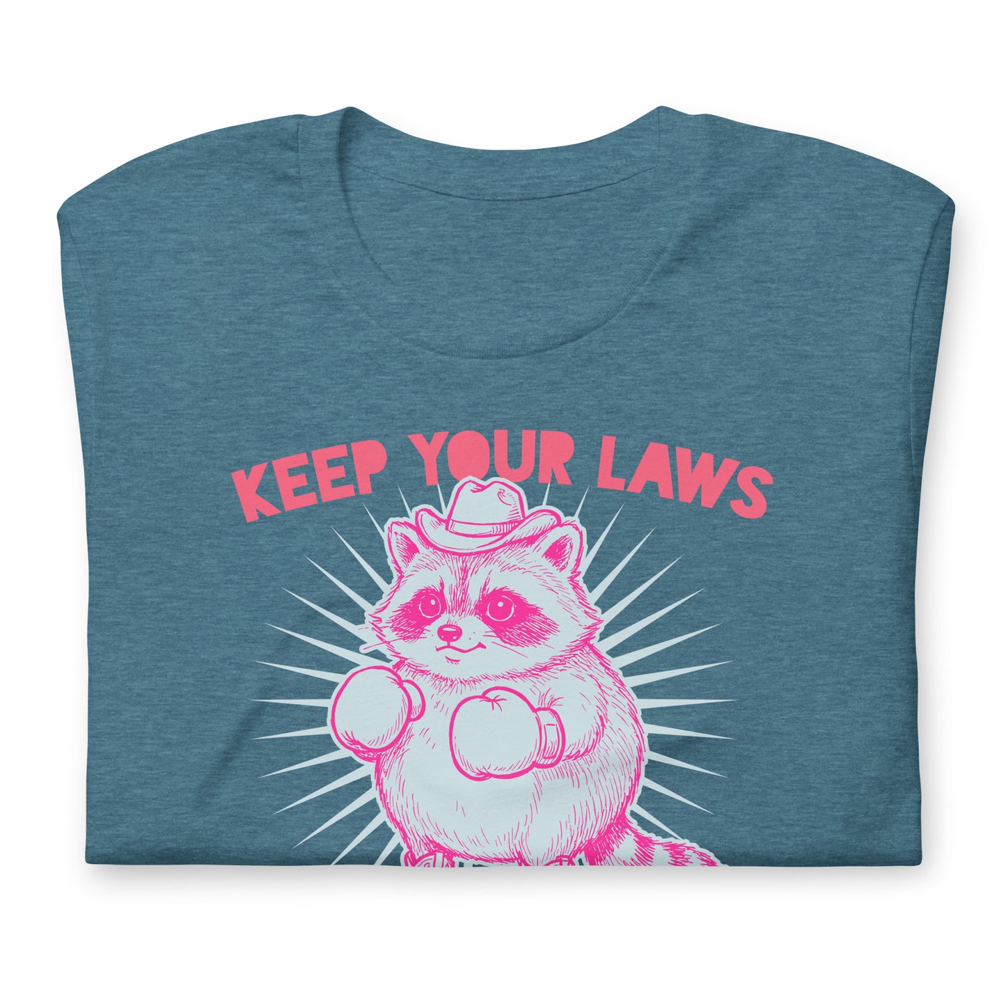 Folded blue heather unisex tee displaying cowboy raccoon illustration with “Keep Your Laws” wording in western feminist activist design.