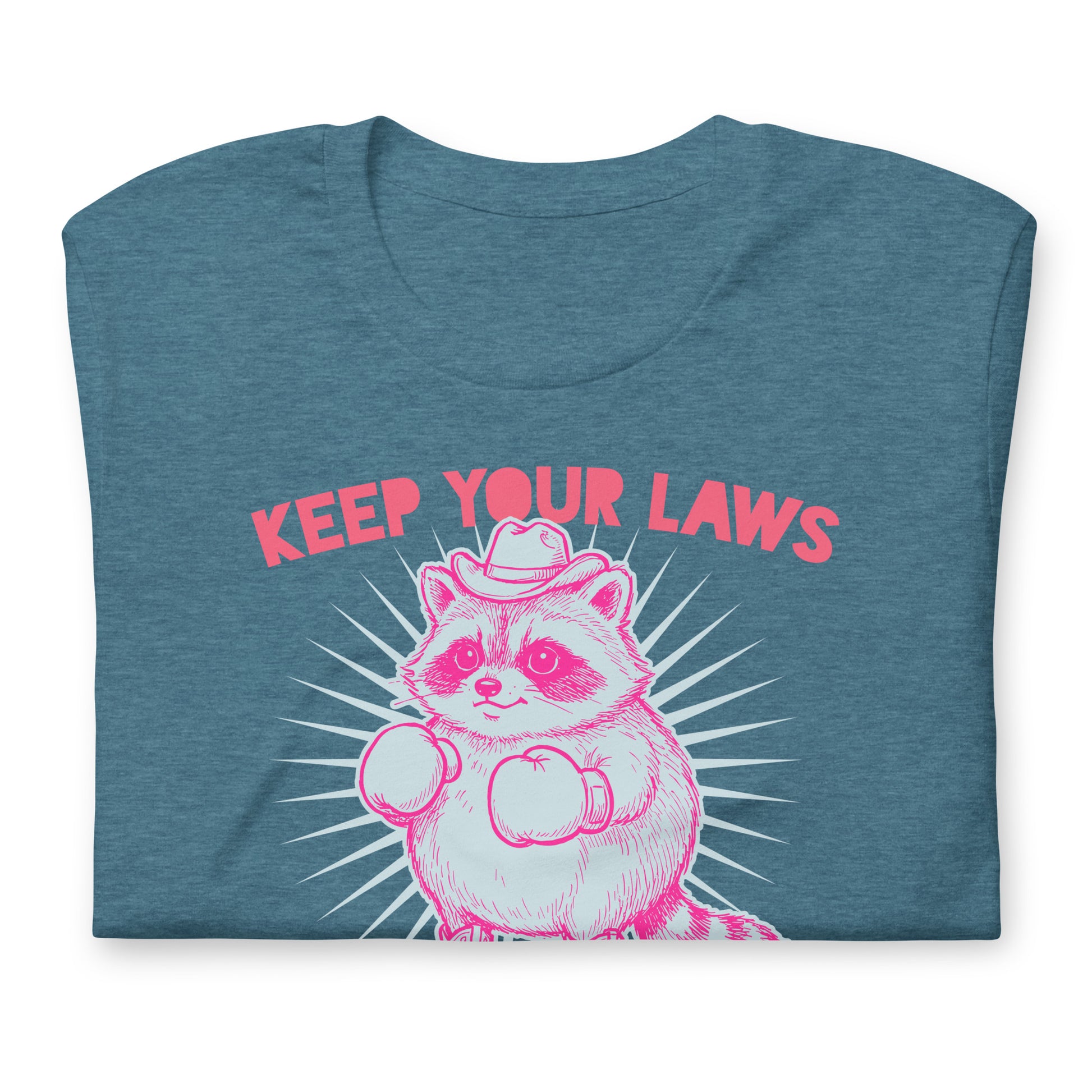 Folded blue heather unisex tee displaying cowboy raccoon illustration with “Keep Your Laws” wording in western feminist activist design.