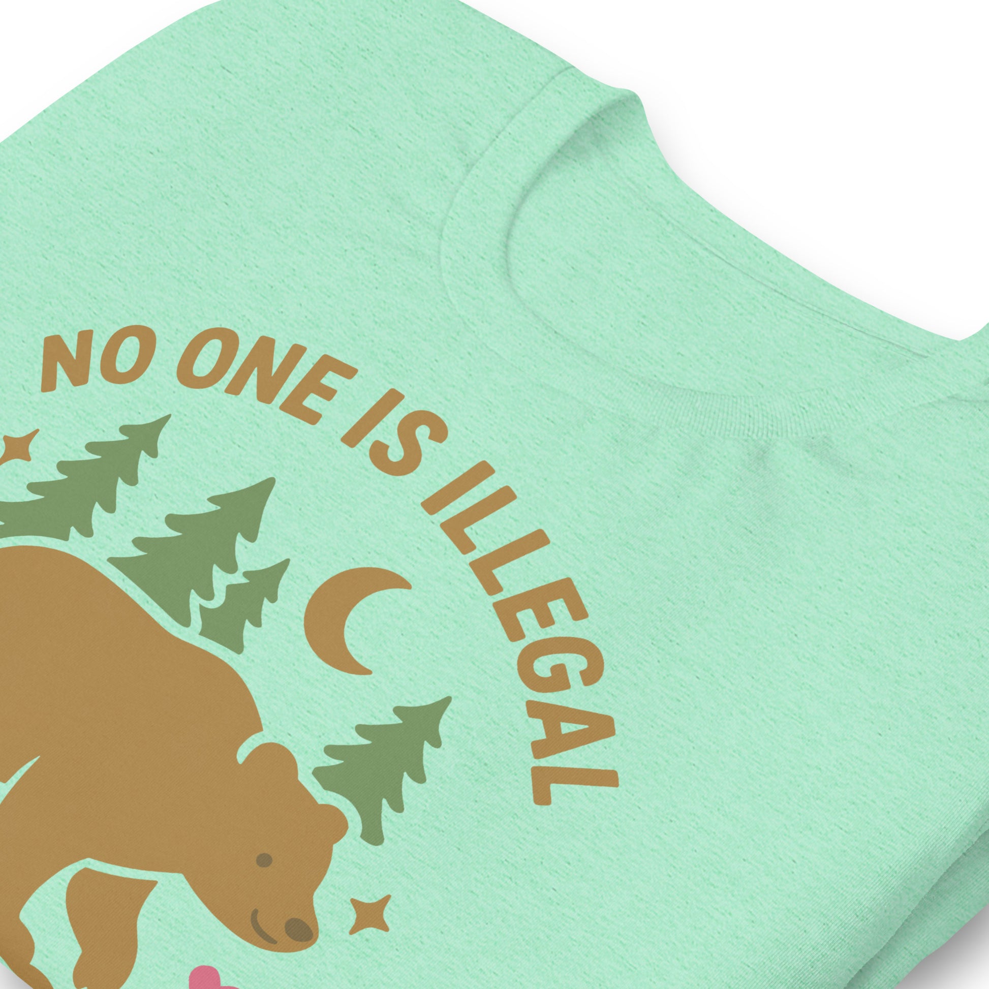 Close-up of a heather mint unisex t-shirt showing the printed bear, moon, and forest art with the phrase “NO ONE IS ILLEGAL ON STOLEN LAND,” highlighting soft fabric texture.