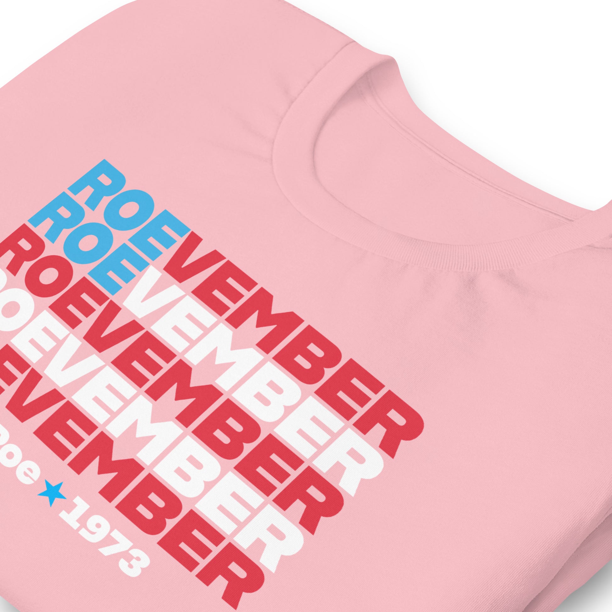 Pink unisex t-shirt close-up featuring stacked red, white, and blue typography reading “Roevember Pro Roe 1973.”