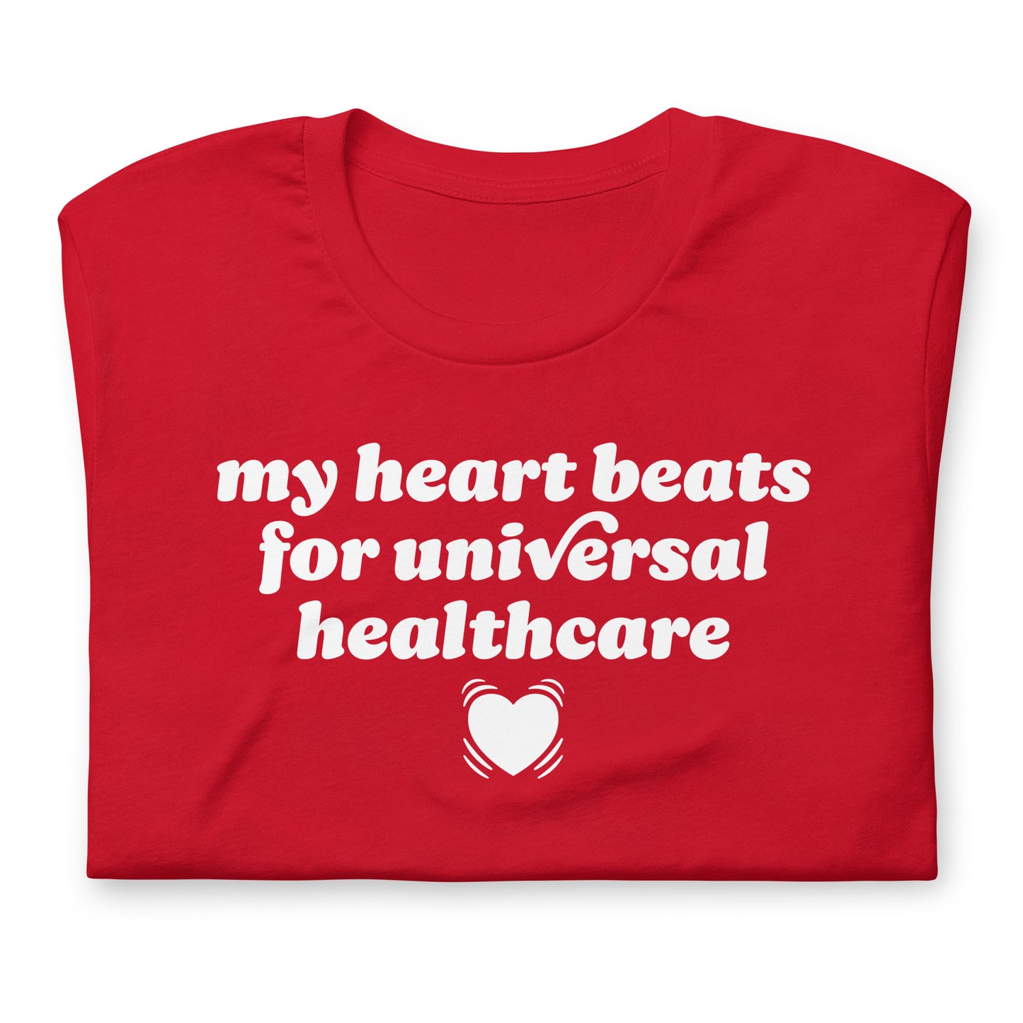 Folded red unisex t-shirt close-up highlighting the phrase “my heart beats for universal healthcare,” showing print texture and Valentine-themed activist apparel styling.