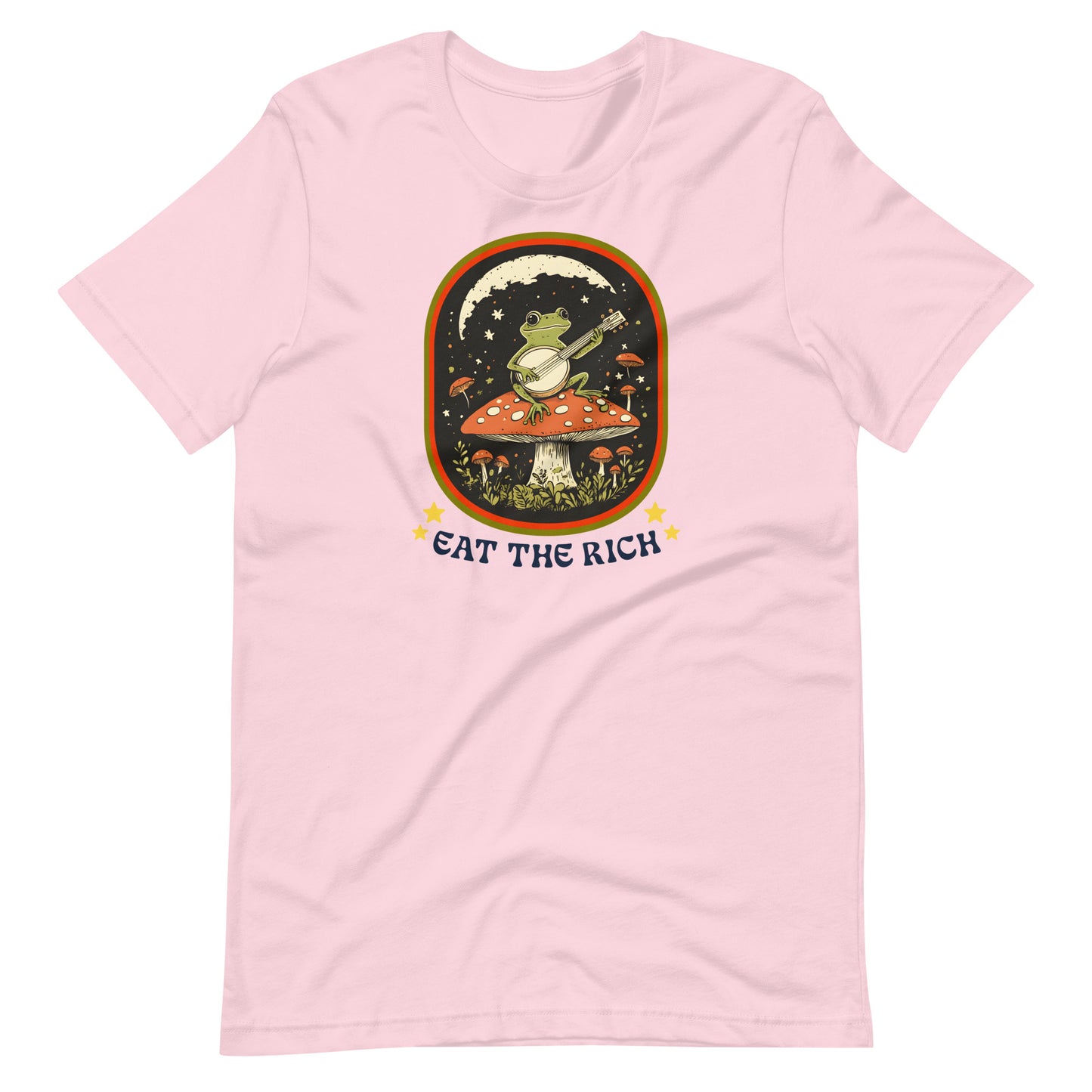 Soft pink unisex t-shirt showcasing a folk-art frog playing a banjo with vintage-inspired “Eat The Rich” anti-capitalist protest artwork.