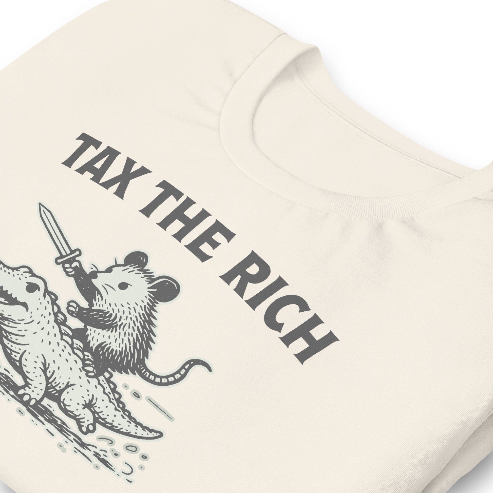 Close-up of vintage white t-shirt featuring a vintage woodcut-style opossum riding an alligator beneath the bold “Tax the Rich” message.