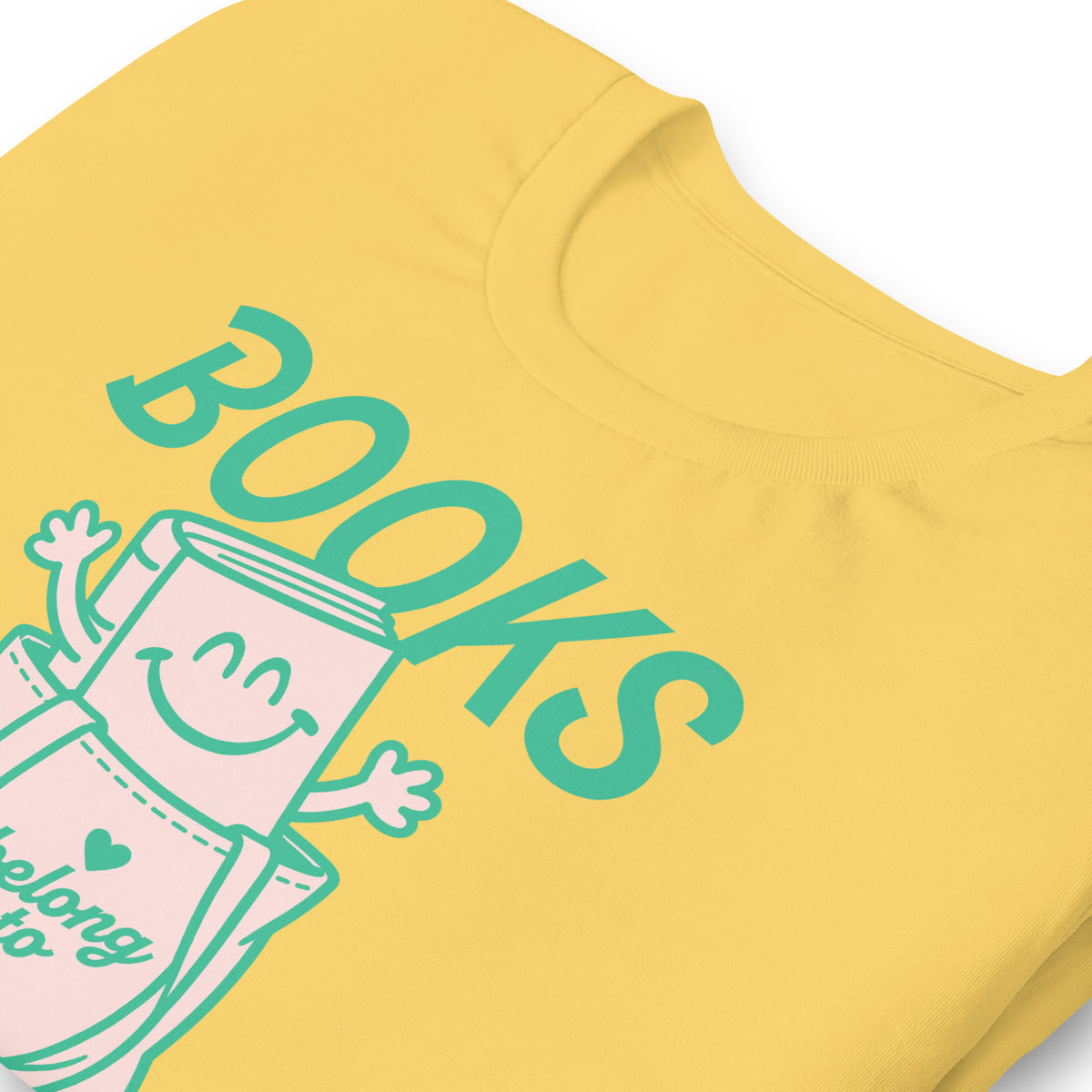 Close-up of the “Books Belong to Everyone” design on a yellow t-shirt, highlighting the playful illustrated book character and teal lettering.
