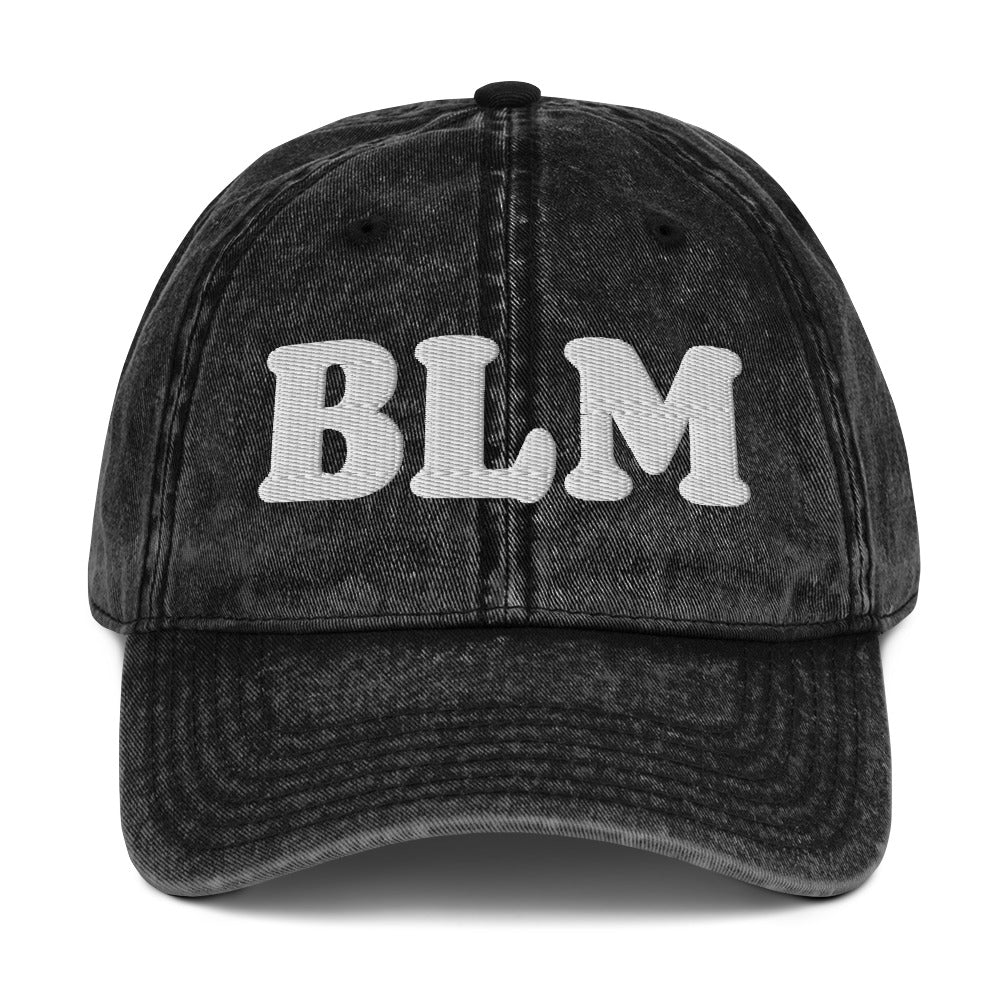 Black vintage cotton twill cap with raised embroidered lettering reading “BLM,” washed fabric texture, curved brim, and classic unstructured dad hat silhouette.