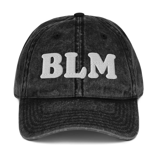 Black vintage cotton twill cap with raised embroidered lettering reading “BLM,” washed fabric texture, curved brim, and classic unstructured dad hat silhouette.
