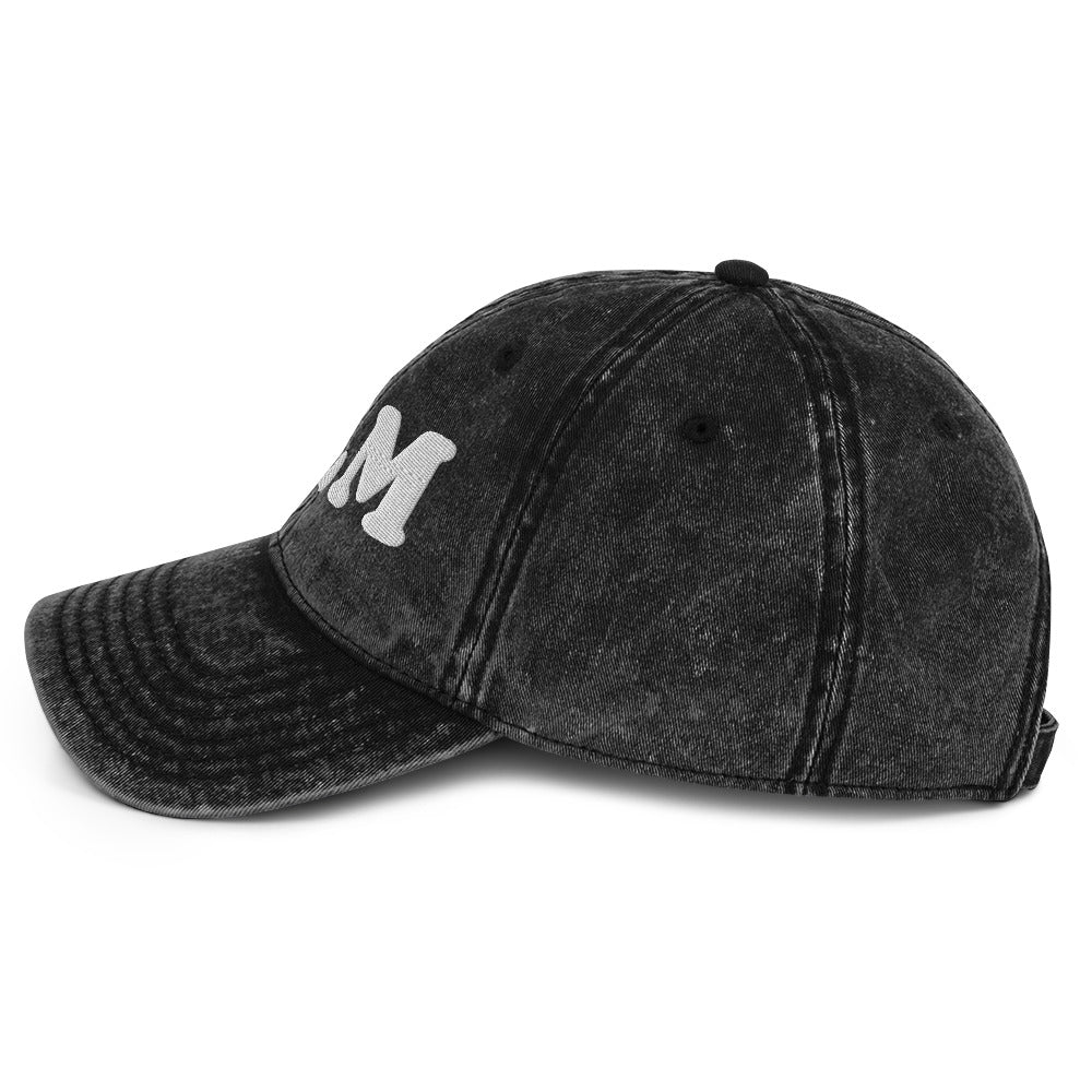 Side angle of a black vintage cotton twill cap featuring raised “BLM” embroidery, curved brim profile, and distressed wash effect on the fabric.