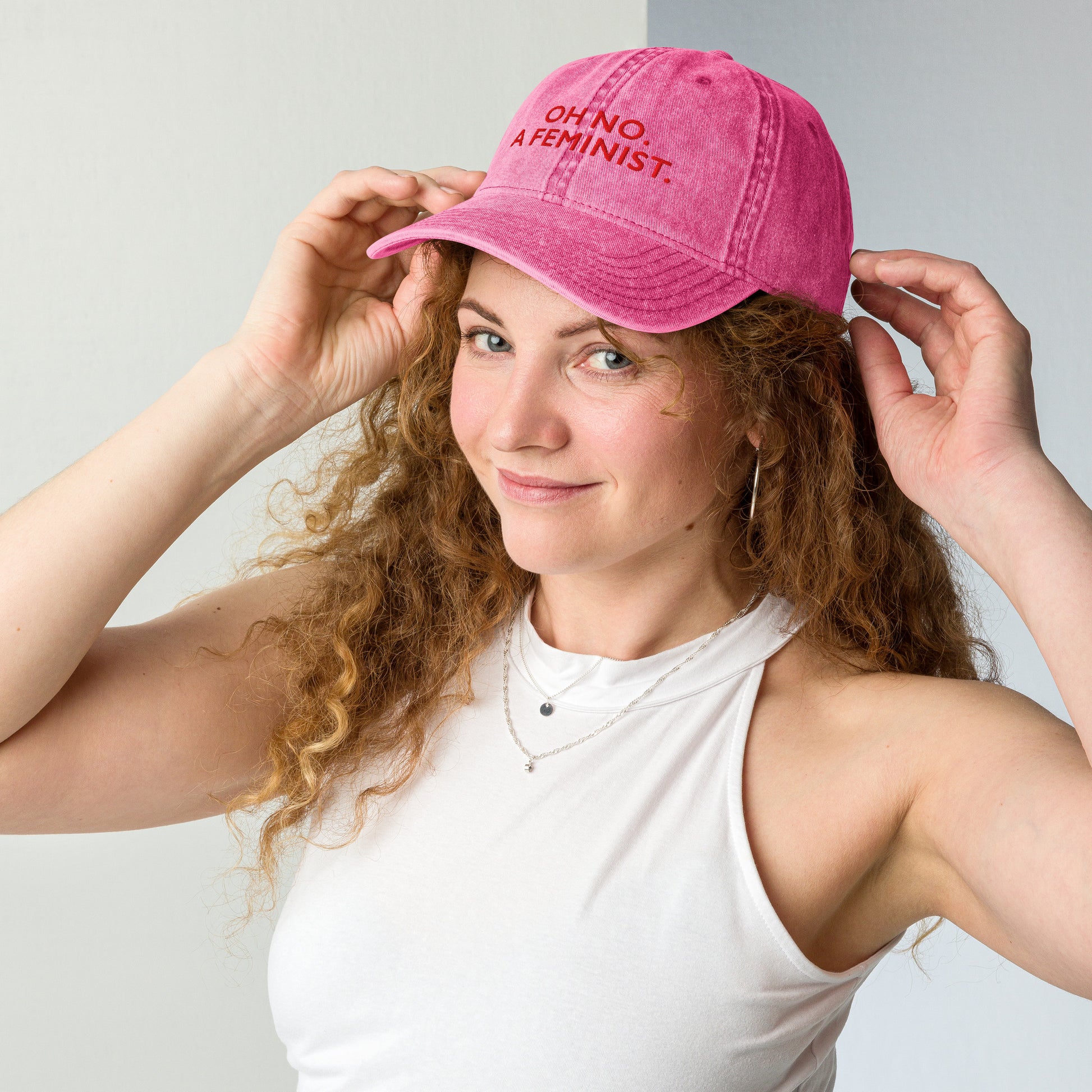 Person adjusting a pink vintage cap embroidered with “OH NO. A FEMINIST.”, showcasing the cap’s classic washed finish and minimalist feminist message.