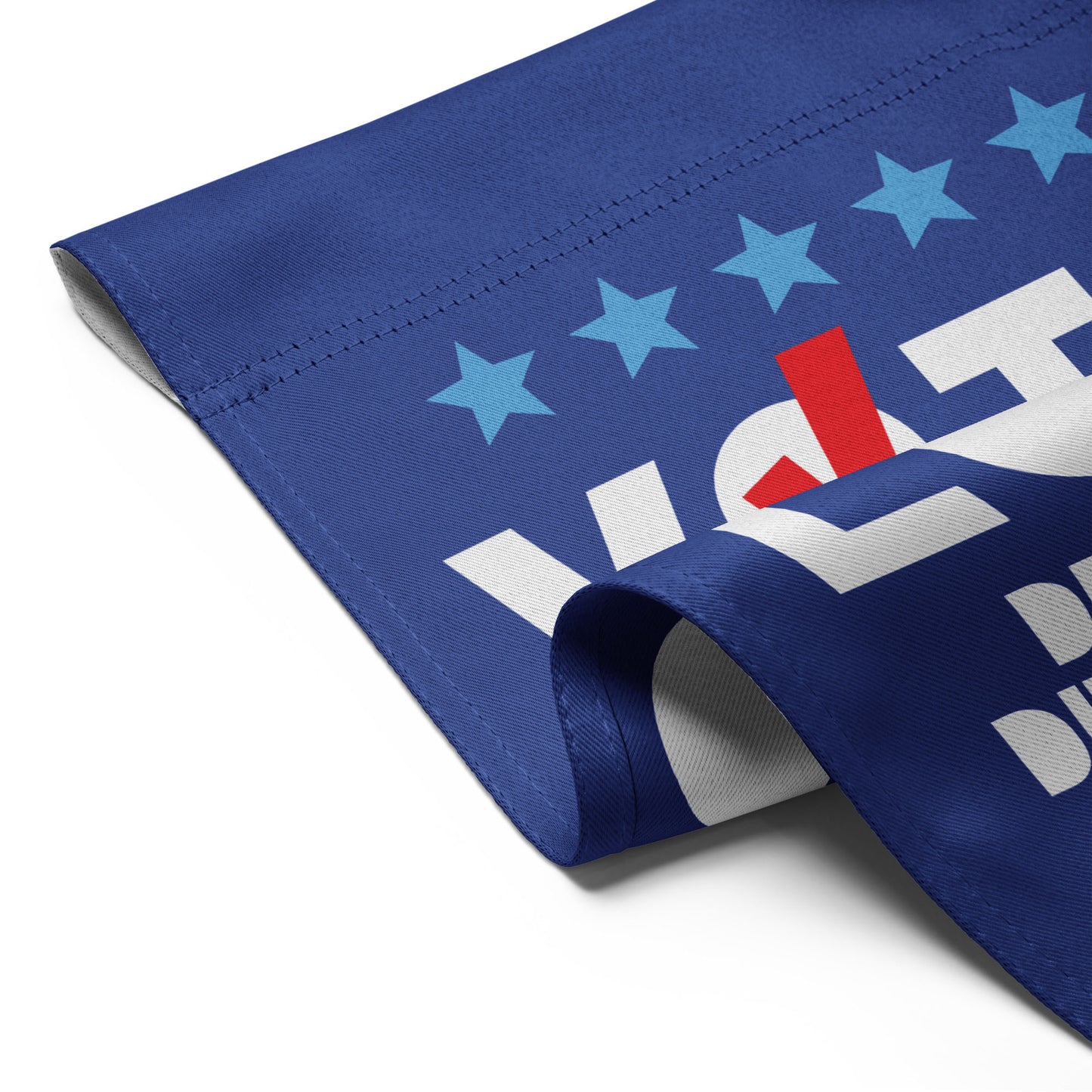 Close-up folded blue garden flag corner showing white “VOTE” lettering, stars, and visible patriotic stripe from the pro-democracy design.