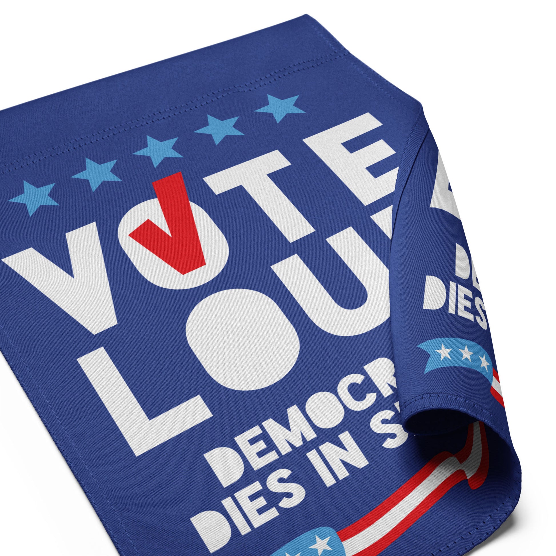 Folded blue garden flag detail featuring oversized “VOTE LOUD” typography with partial democracy phrase in patriotic outdoor activism design.