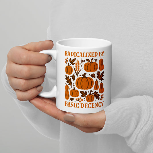 White ceramic mug with “Radicalized by Basic Decency” pumpkin and leaf design, cozy progressive fall drinkware for activists.