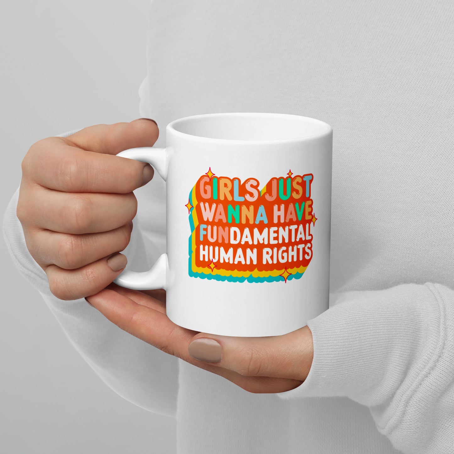 White ceramic mug with groovy retro orange-and-teal “Girls Just Wanna Have Fundamental Human Rights” graphic, held in both hands.