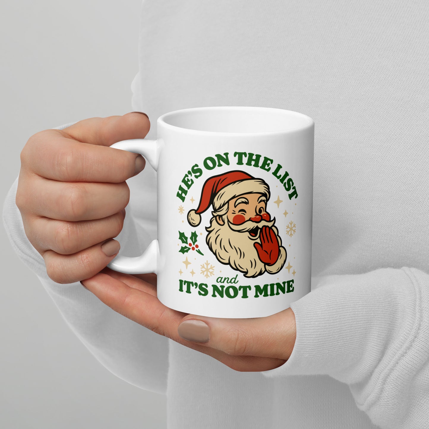 11oz white ceramic mug held in both hands, featuring a retro-style Santa winking with the text “He’s On the List & It’s Not Mine,” surrounded by small festive snowflakes and stars.