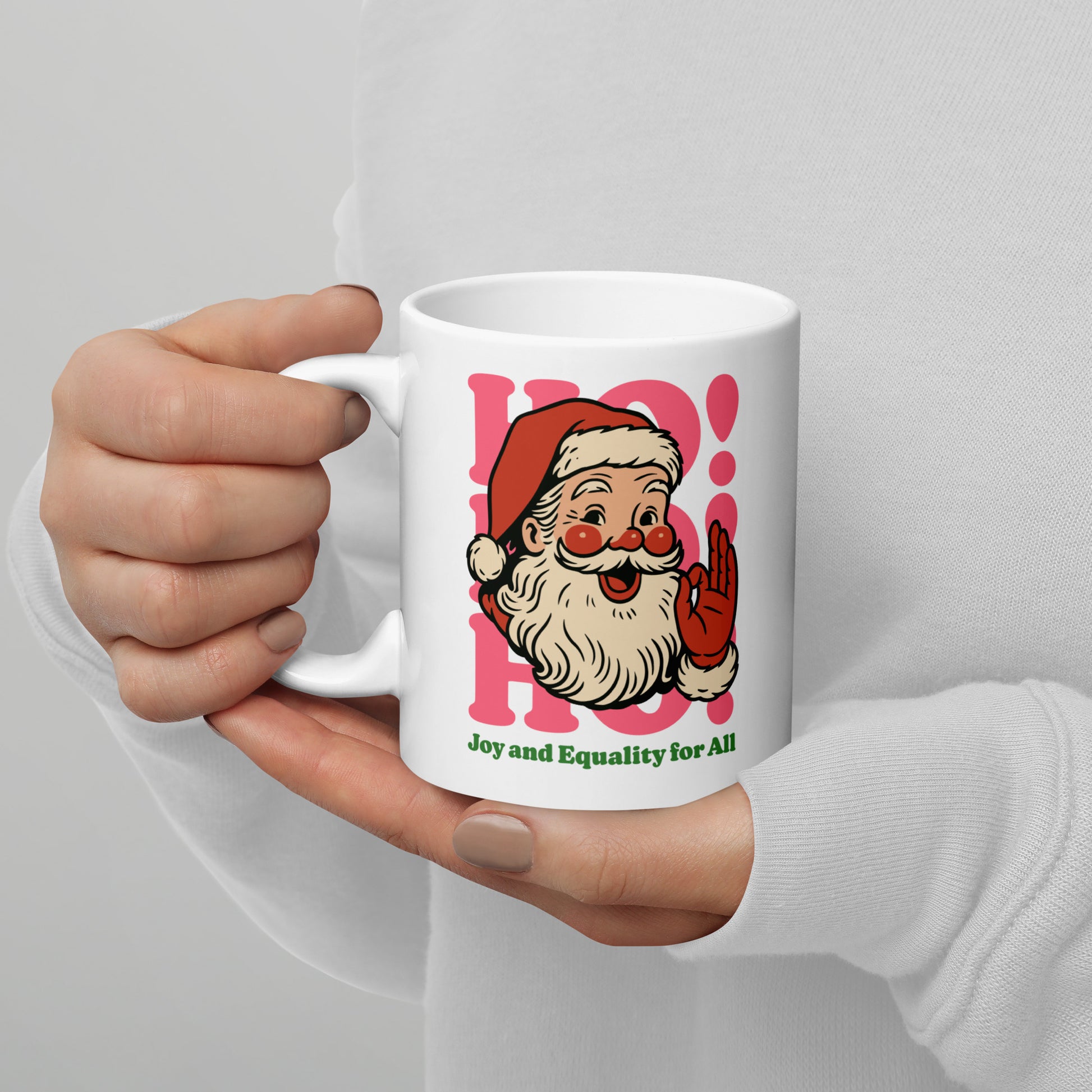 Close-up of a person holding the 11 oz white ceramic mug featuring a retro Santa illustration with pink shapes and the phrase “Joy and Equality for All.”