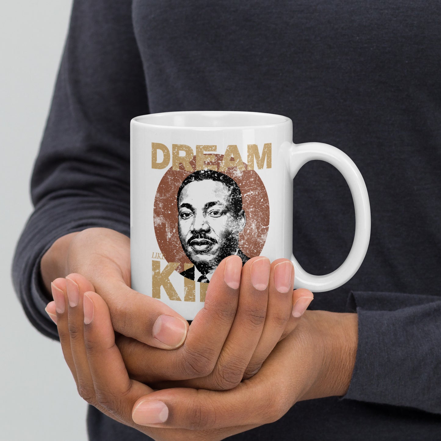 Side view of hands presenting a white 11 oz mug with the worn “DREAM LIKE KING” text and MLK portrait inside a rustic circle. Retro activist-inspired design from Blue Wave USA.