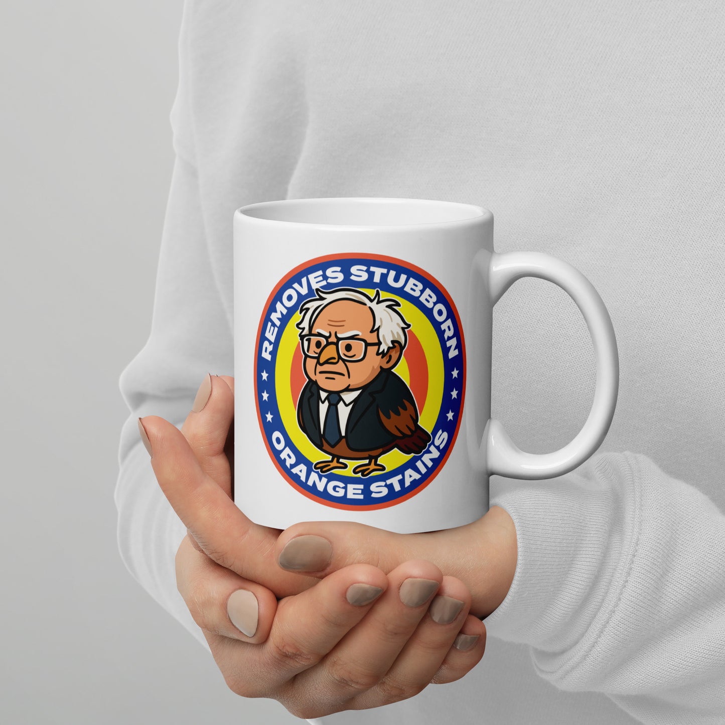 White mug featuring Birdie Sanders parody detergent badge with “Removes Stubborn Orange Stains” text, playful political humor drinkware for progressive gift shoppers.