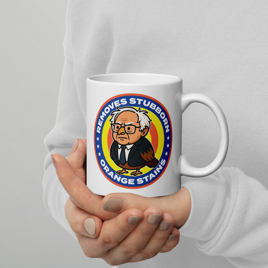 White mug featuring Birdie Sanders parody detergent badge with “Removes Stubborn Orange Stains” text, playful political humor drinkware for progressive gift shoppers.