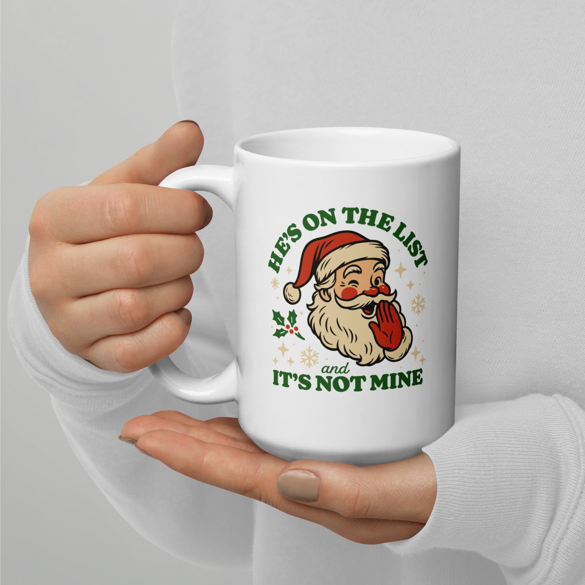15 oz white ceramic mug held with both hands, showing the retro Santa face and the cheeky holiday phrase in green lettering.