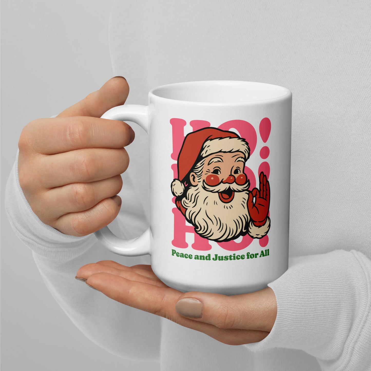 15 oz white ceramic mug held in both hands, displaying a retro Santa illustration with pink “HO!” typography and the printed phrase “Peace and Justice for All.”