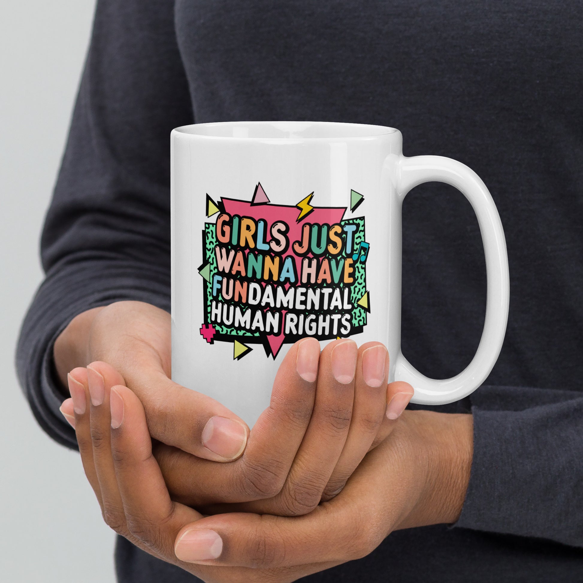 White “Girls Just Wanna Have Fundamental Human Rights” mug shown from the front, featuring pastel lightning bolts and playful shapes for a bold activist statement.