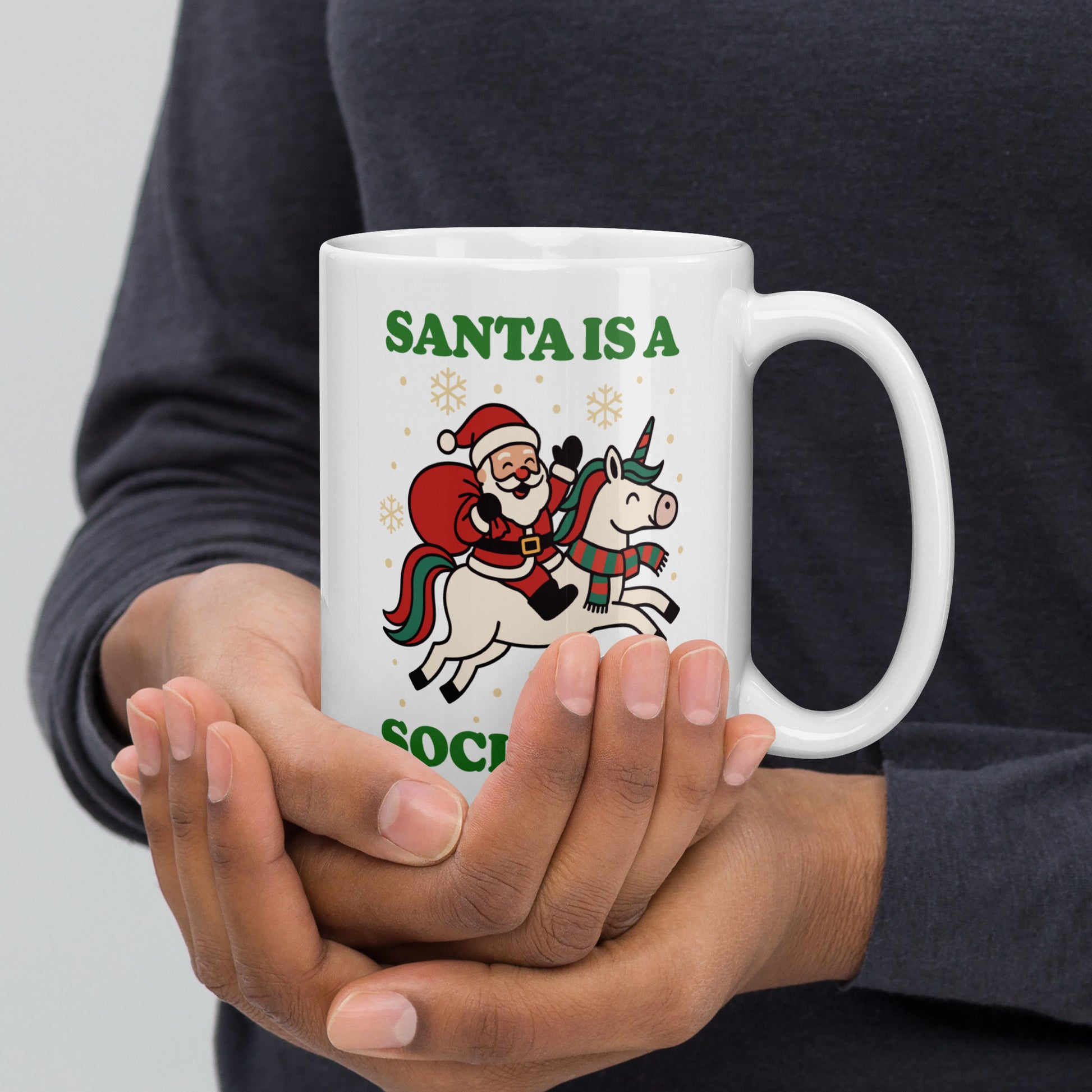 White 15 oz ceramic mug held in both hands displaying a retro Santa riding a unicorn with holiday stars and the printed phrase “SANTA IS A SOCIALIST.”