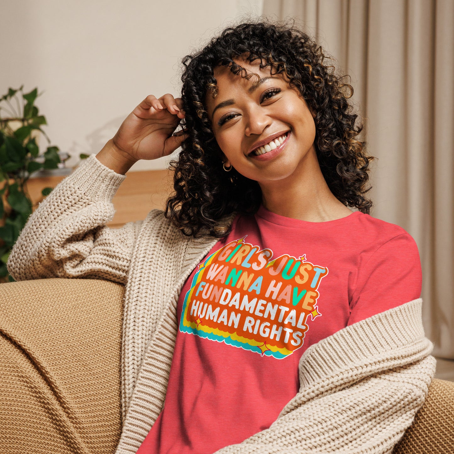 Model sitting comfortably in a heather red “Girls Just Wanna Have Fundamental Human Rights” t-shirt. Cozy, progressive design for everyday wear.