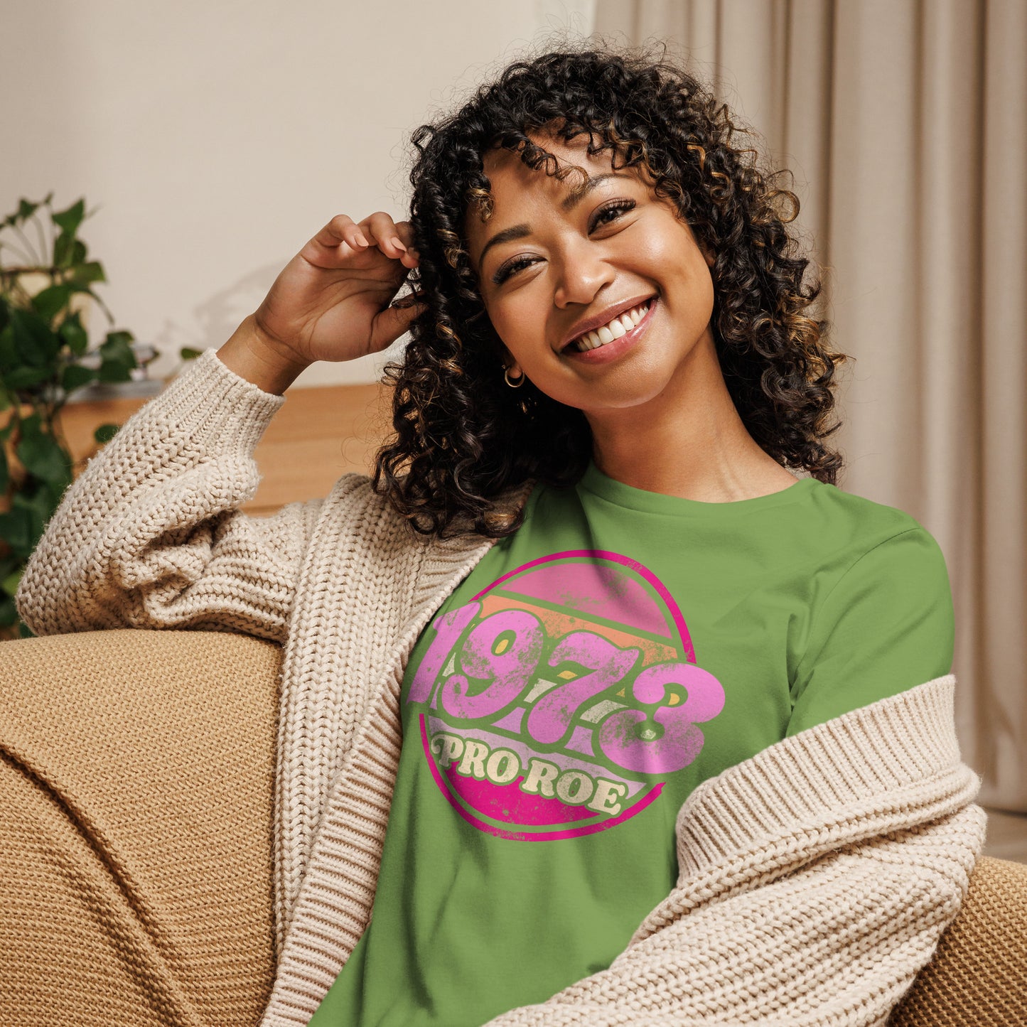Model wearing a green women’s relaxed t-shirt with a retro pink circular “1973 PRO ROE” graphic, casual lifestyle styling shown indoors from Blue Wave USA.