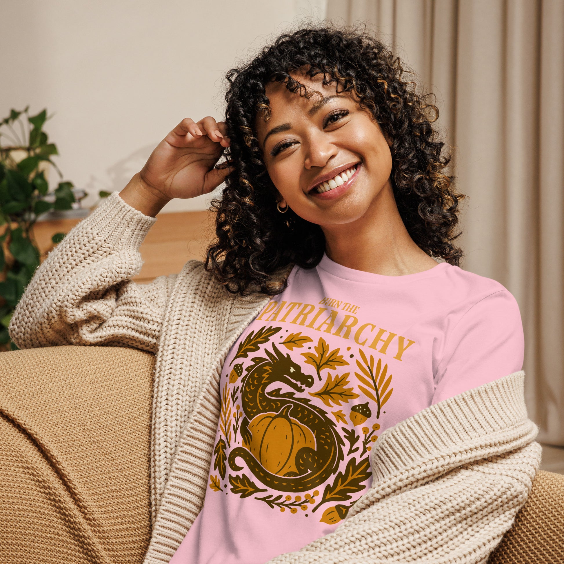 Smiling woman in pink “Burn the Patriarchy” feminism dragon t-shirt, cozy activist fashion for Thanksgiving season.